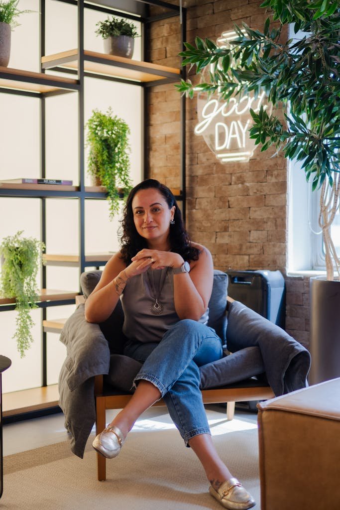 A woman sitting comfortably in a modern room with decorative plants and a neon sign.